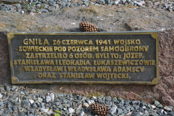 Bronze memorial plaque mounted on a rough rock, with a pinecone on top and Polish inscription describing wartime victims.