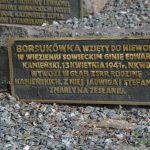 Bronze memorial plaque with Polish inscription mounted on a rough stone base, set among gravel and small rocks.