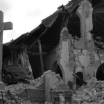 Crucifix stands amid rubble and the ruins of a collapsed church, with shattered brick arches and debris scattered around.